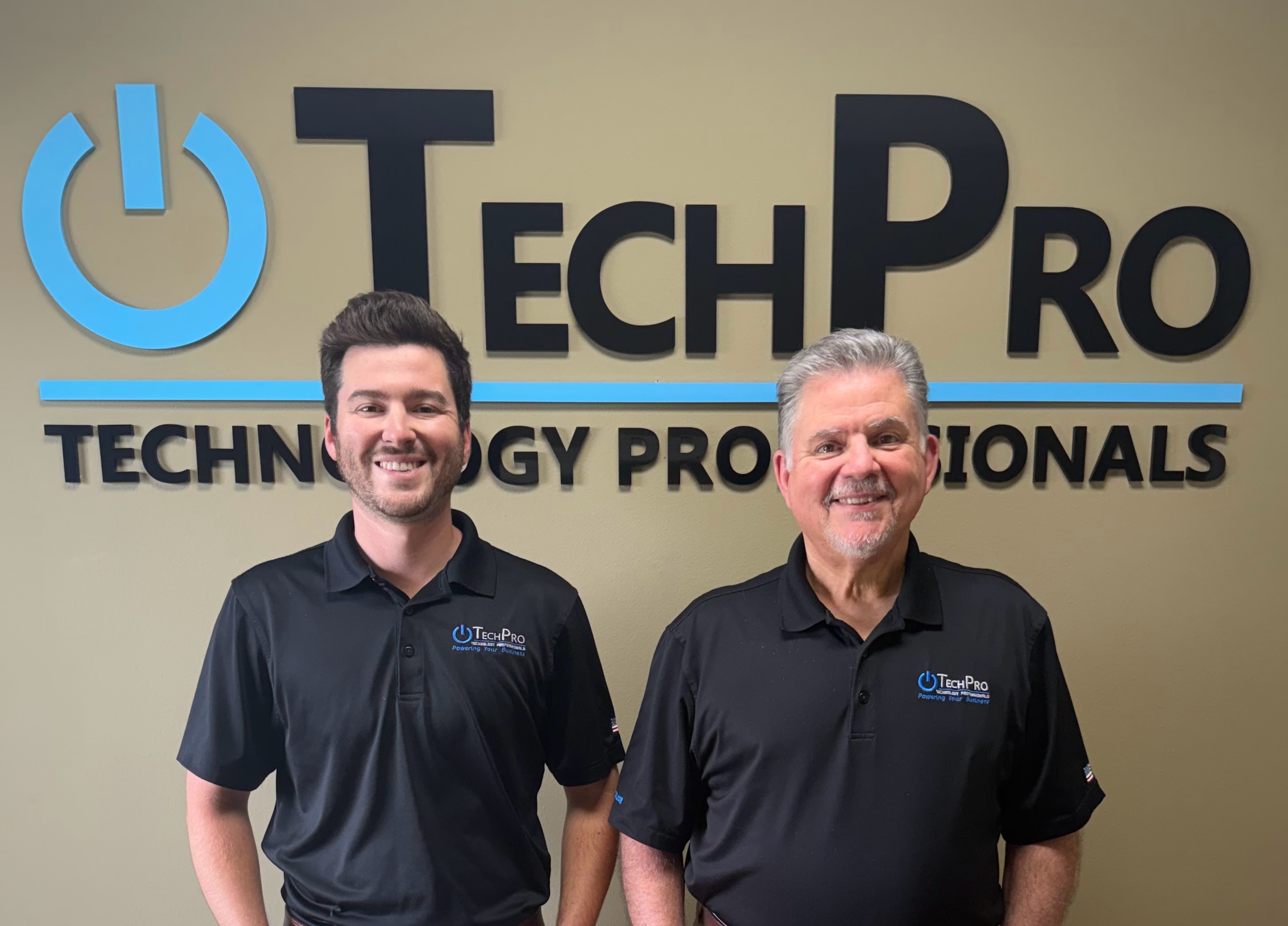 Two TechPro team members standing in front of the TechPro office sign